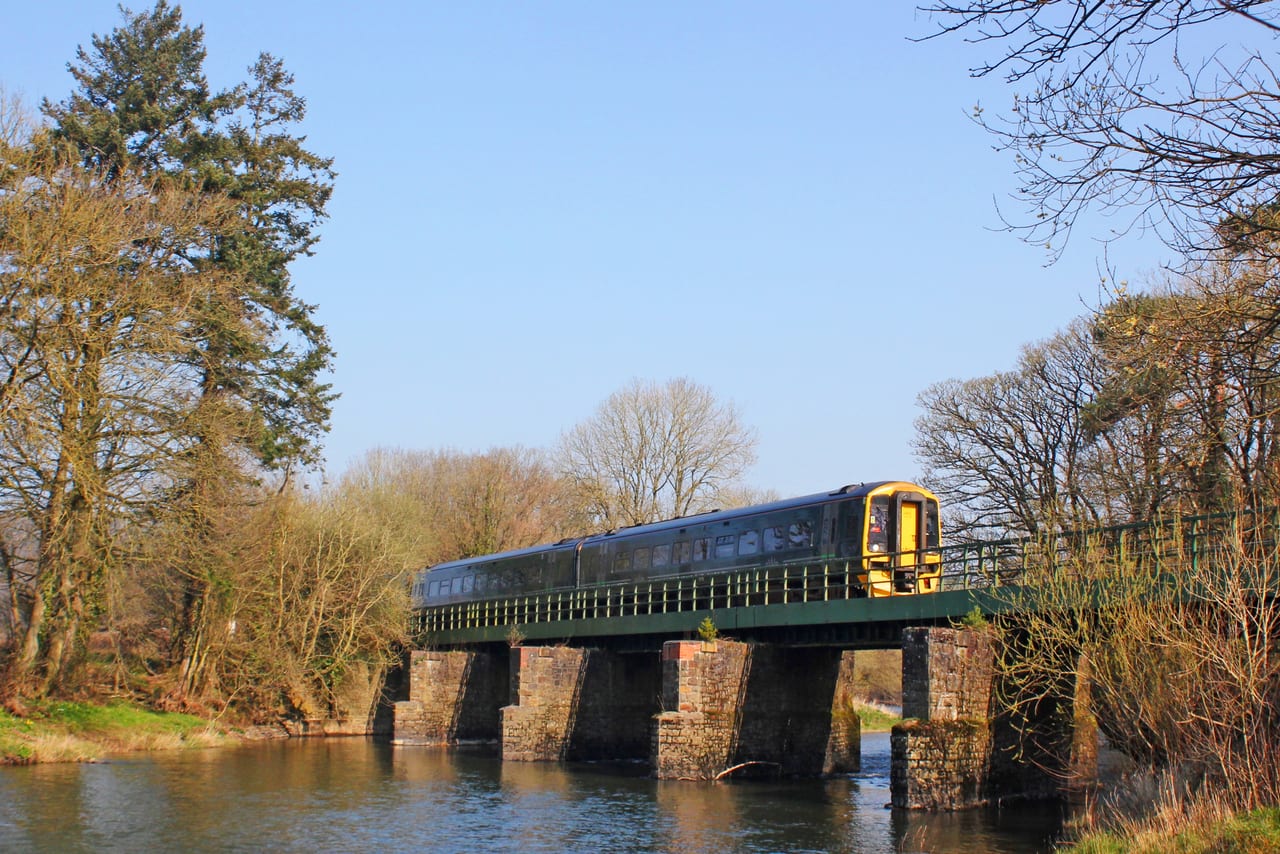A two-car train crossing the River Taw viaduct at Umberleigh on its masonry piers